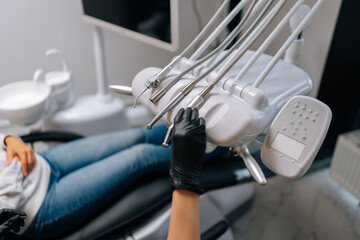 Close-up side view of unrecognizable female stomatologist in rubber gloves taking electrical dental drill from set of dental tools to treat patient with toothache, in modern dentistry clinic.