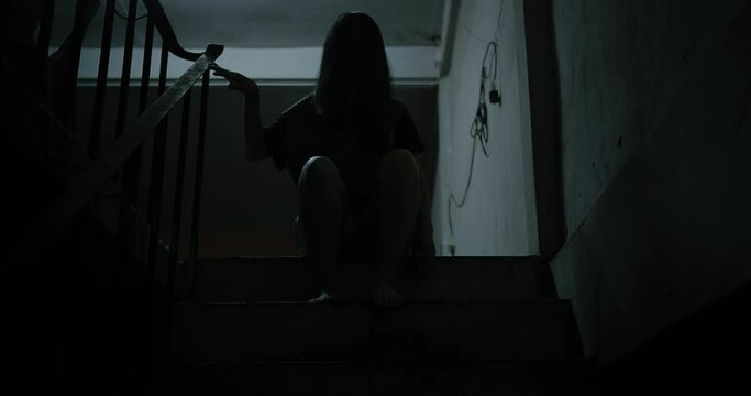 Horror scene of a mysterious Scary Asian ghost woman creepy have hair covering the face sitting on staircase at abandoned house with background dark scene movie at night, festival Halloween concept