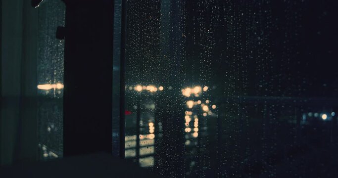Torrential storm rain fall on street lights at night behind wet window, static shot