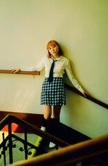 A cute ginger Asian student in uniform is standing on a university staircase. Diversity,...