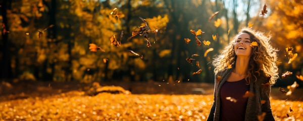 Joyful smiling Woman throwing leaves into the air in a park in the autumn. Colors are warm orange and yellow. Concept of fall colors, fashion and happiness. Shallow field of view. - Powered by Adobe