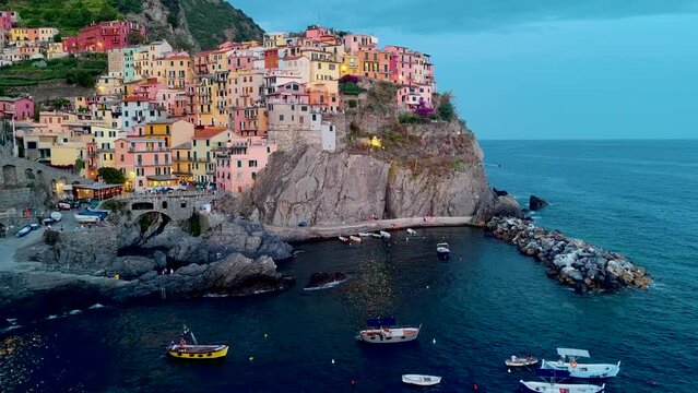 Aerial 4K footage on Manarola town with many colorful houses and bay with small boats in Cinque Terre during a sunset