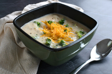Eating a bowl of cream of broccoli soup topped with cheddar cheese.