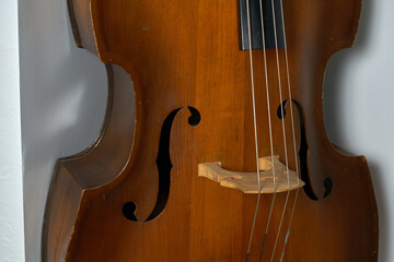 An old double bass leaning on a white wall.