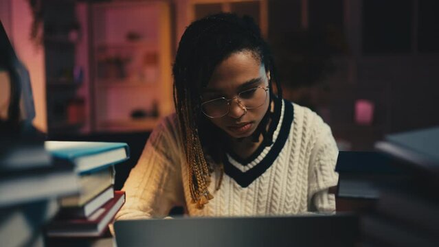 Young woman doing dull office work behind desk with stacks of books, studying