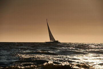 The view of sailboat is heeling at sunset, reflection of sun on water surface