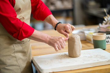 Unrecognizable woman cutting clay with thread standing behind table in studio.