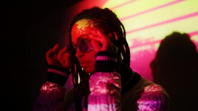 Stylish young African American woman standing on synthwave background, 80s mood