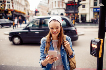 Young woman using a smart phone while crossing the street in london