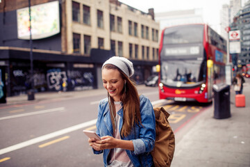 Young woman using a smart phone while waiting for her bus at a bus stop in London
