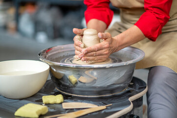 Woman working on potter's wheel in a pottery workshop, creating clay pot.