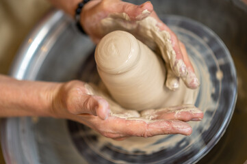 Woman working on potter's wheel in a pottery workshop, creating clay pot.