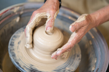 Woman working on potter's wheel in a pottery workshop, creating clay pot.