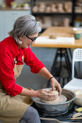 Woman potter molding pot shape on pottery wheel at her workshop.