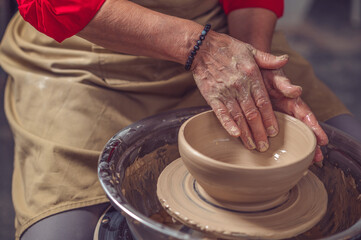 Woman working on pottery wheel and sculpting clay plate.