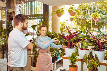 beautiful caucasian female employee owner helping or showing plants to a customer in a small plant business