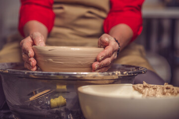 Woman potter creating beautiful plate with clay, making works of art with his hands.