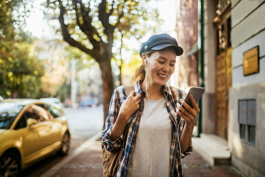 Young woman using a smart phone while walking on the sidewalk in a city