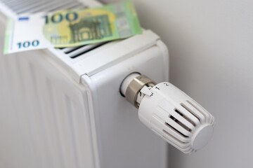 Rising cost of heating and electricity in Europe. Heating radiator with thermostat on which euros lie. Rising energy prices. Energy crisis and recession. 2 euro coins and 100 euro banknotes