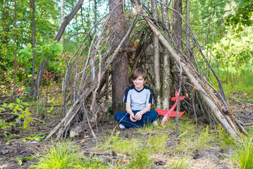 a happy 10 year old boy sits in a makeshift hut made of branches. joyful child spends summer holidays in a camp in nature © Ruslan Russland