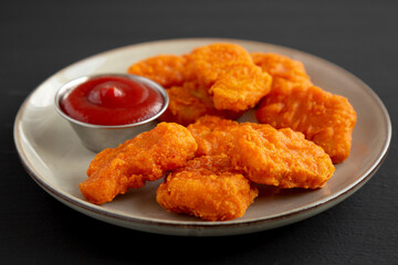 Homemade Spicy Chicken Nuggets on a Plate on a black background, side view.