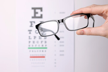 vision correction glasses in hand against the background of a vision test table with space for text