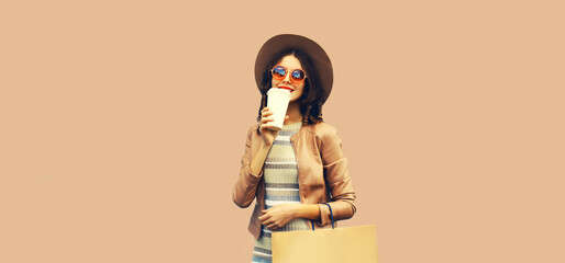 Portrait of beautiful happy smiling woman with shopping bags and cup of coffee wearing jacket, round hat on brown background