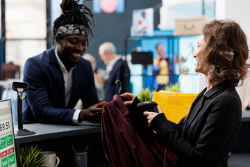 Elegant customer talking with manager at cash register, making transaction on pos terminal in shopping center. Boutique employee scanning shirt using store scanner, commercial activity.