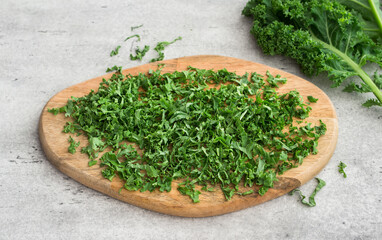 Wooden board of chopped curly kale on gray textured background. Cooking a delicious healthy meal