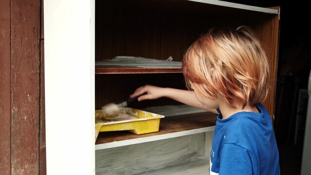 A young boy paints an old wardrobe. Children's creativity, furniture restoration. Brush painting.