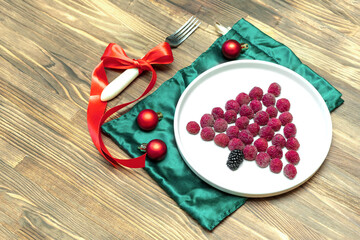 Funny Christmas tree shaped sweet fresh raspberry berry on plate on wooden background for kids children breakfast. xmas food with new year decorations copy space