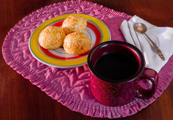 Wooden table with delicious cheese breads, a coffee mug, white napkin and a sugar spoon on a place mat