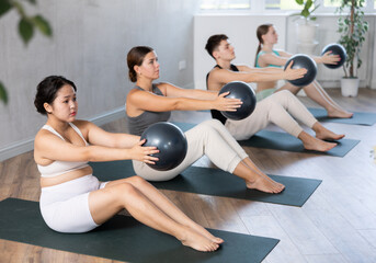 Portrait of happy young people wearing activewear working out doing softball pilates indoors in fitness studio.