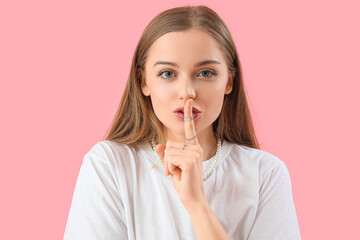 Young woman showing silence gesture on pink background, closeup