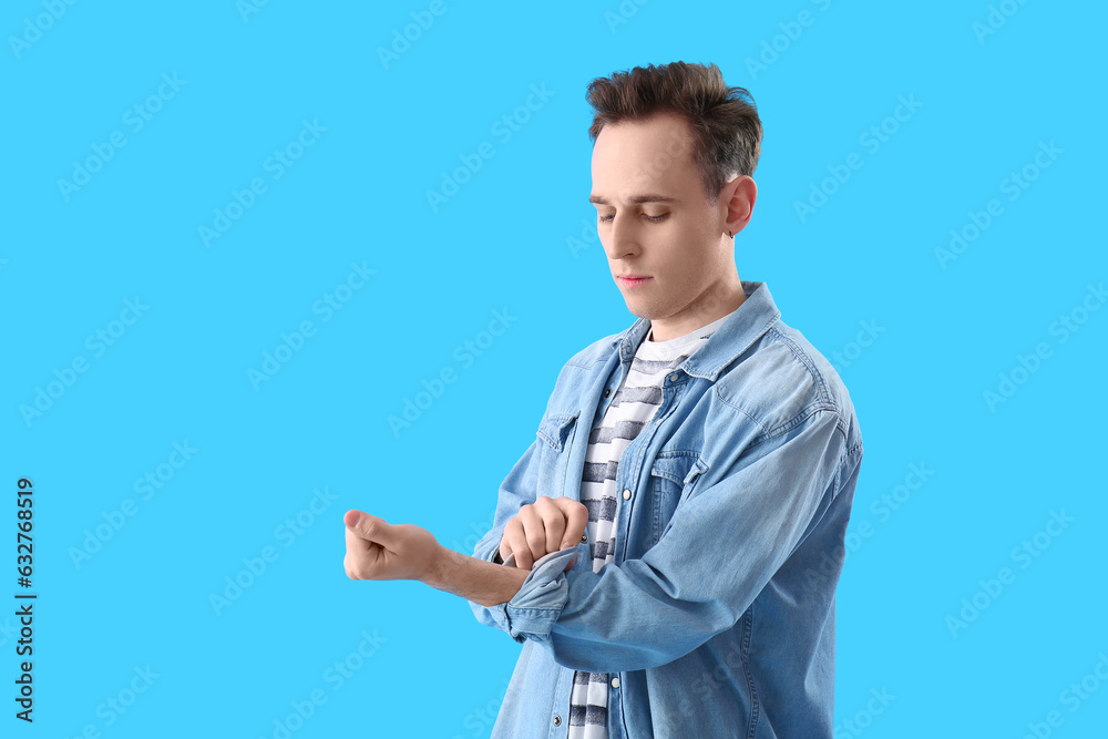 Wall mural Young man rolling up his sleeve on light blue background - Wall murals