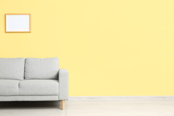 Stylish grey sofa near yellow wall