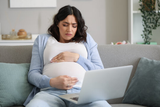 Tired young pregnant woman working with laptop at home