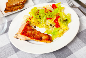 Grilled salmon steak with fresh lettuce salad served on table.