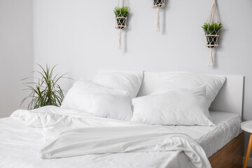 Large double bed with white pillows and houseplants in interior of light bedroom