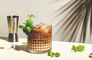 Mint White Russian cocktail drink with vodka, coffee liqueur, mint schnapps, cream and ice cubes on beige background, hard light, shadow pattern