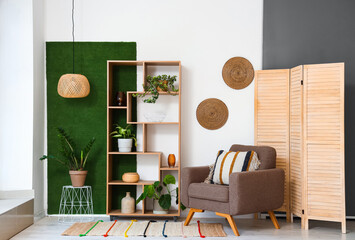 Interior of light living room with brown armchair, wicker lamp and shelving unit
