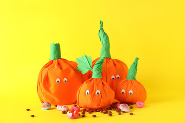 Paper pumpkins for Halloween and tasty candies on yellow background