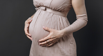 pregnant woman touching her belly on gray background