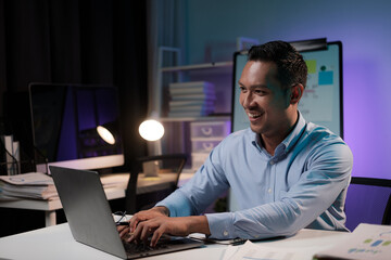 Smiling businessman working with laptop computer in the office room during the night, working overtime.