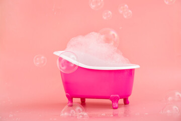 Small bathtub with soap foam and bubbles on pink background