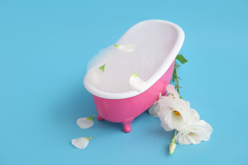 Fototapeta na wymiar Small bathtub with soap foam and beautiful eustoma flowers on color background