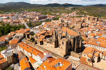 Fototapeta na wymiar Drone view of picturesque cityscape of historical part of Placencia surrounded by ancient fortress wall overlooking tiled roofs of houses and medieval gothic cathedral on sunny spring day, Spain
