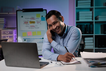 Smiling Asian businessman having a phone call with his team discussing the project at night time.