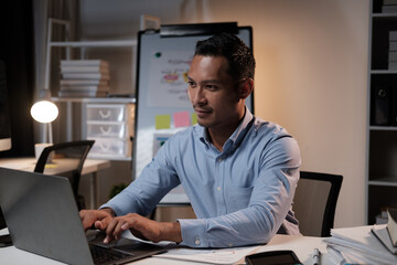 Naklejka premium Portrait of young Asian businessman working on his project with laptop computer, working overtime at night in the office room.