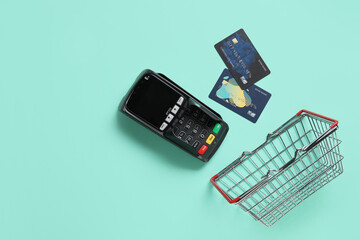 Shopping basket with payment terminal and credit cards on turquoise background